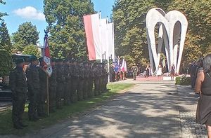 Od prawej strony żołnierze stojący w dwuszeregu , po prawej stronie przedstawiciele służb i władz samorządowych. Po środku widoczny pomnik Lotników Polskich, obok po prawej stronie flaga polski.