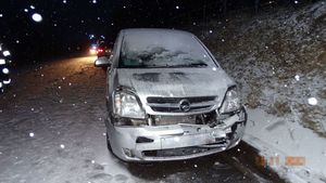 Pojazd opel kolor srebrny metalik z rozbitym przednim zderzakiem stoi  na poboczu, , w tle widoczny pojazd Straży Pożarnej na sygnałach,widoczne opadające płatki  śniegu.