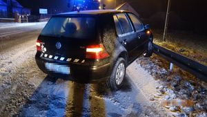 Pojazd volkswagen kolor ciemny stoi przednim kołem na barierze energochłonnej pozostałe koła na jezdni,widoczne opadające płatki  śniegu.