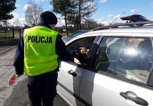 Policjantka ruchu drogowego trzyma w uchylonej szybie samochodu osobowego urządzenie do pomiaru stanu trzeźwości.