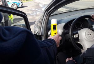 Otwarte drzwi samochodu policjant w ręce trzyma urządzenie pomiarowe na wyświetlaczu wynik badania  0,00.
