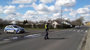 Policjant ruchu drogowego stoi na jezdni. Podaje tarczą uniesioną nad głową sygnał do zatrzymania się jadącemu pojazdowi.