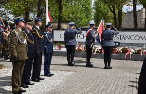 Policyjny poczet sztandarowy składa pokłon w stronę Pomnika Powstańców Śląskich, po lewej stronie stoją komendanci i dowódcy służb z uniesionymi prawymi dłońmi w geście oddania honoru.