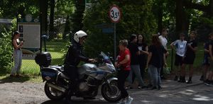 Policjant w białym hełmie ochronnym siedzi na motocyklu i rozmawia z jedną z organizatorek biegu. W tle uczestnicy zawodów.