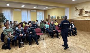 Sala lustrzana Miejskiego domu kultury w Oleśnie. Umundurowany policjant prowadzi pogadankę z seniorami. Słuchacze siedzą przed policjantem na krzesłach ustawionych w kilku szeregach.