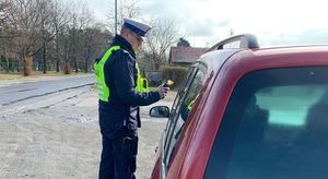 Policjant ruchu drogowego podaje kierowcy urządzenie do pomiaru stężenia alkoholu w wydychanym powietrzu.