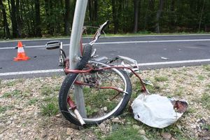 Zdeformowany rower owinięty wokół słupka - znaku drogowego, w tle jezdnia na której widać czerwony pachołek ostrzegawczy.