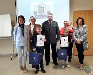 Zdjęcie grupowe opiekunowie - wychowawcy oraz mamy wyróżnionych uczniów pozują do wspólnego zdjęcie w tle logo KPP w Oleśnie wyświetlone na rzutniku .