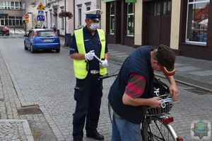 Policjant ruchu drogowego stoi obok rowerzysty, który zakłada odblaskowa opaskę na rowerowym bagażniku.