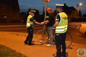 Policjantka ruchu drogowego zakłada odblaskowa opaskę na rękę rowerzysty obok stoi drugi policjant.