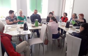 Uczestnicy debaty siedzą przy stole, wśród nich I Zastępca Komendanta Powiatowego Policji w Oleśnie. Na stołach widoczne termosy i filiżanki z kawą i butelki z wodą oraz kartki papieru.