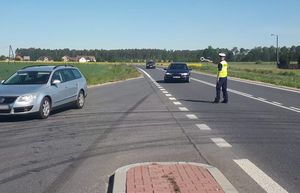 Policjant daje znak do zatrzymania dla nadjeżdżającego ciemnego pojazdu osobowego.