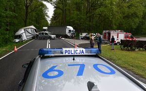 Miejsce wypadku widoczne z nad dachu radiowozu. W tle rozbite dwa samochody ciężarowe, dwie osobówki, wóz bojowy straży pożarnej, ambulans oraz ludzie stojący na poboczu.