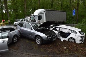 Miejsce wypadku. Na pierwszym planie trzy samochody osobowe. Jeden biały doszczętnie uszkodzony. Za nimi uszkodzony samochód ciężarowy i osobowy. Obok tych pojazdów strażacy.