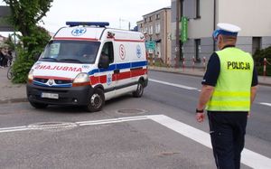 Policjant drogówki kieruje ruchem na skrzyżowaniu. Przed nim przejeżdża ambulans zamykający bieg.