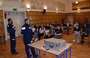 Dwóch policjantów prowadzi prelekcję. Przed nimi na krzesłach siedzą uczniowie.