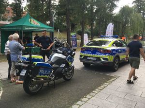 Fragment oleskiej promenady stojący  motocykl i radiowóz policyjny, obok stojący umundurowany policjant.