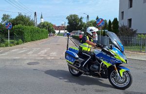 Policjant ruchu drogowego na motocyklu pilotuje biegaczy podczas biegu ulicami Dobrodzienia.