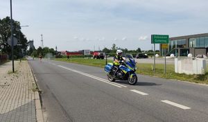 Ulica Oleska w Dobrodzieniu. Policjant na motocyklu pilotuje uczestników biegu.