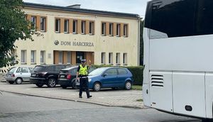 Policjant ruchu drogowego pomaga kierowcy autokaru podczas cofania. w tle Dom Harcerza.