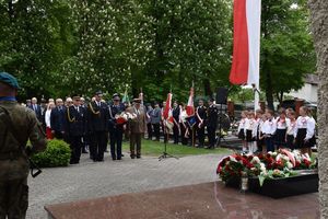 Zdjęcie w kolorze przedstawia delegacje ustawione naprzeciw pomnika Lotników Polskich w Olesnie. Po prawej stronie biało czerwona flaga.