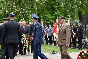 Zdjęcie w kolorze przedstawia delegację Komendantów Policji, strazy Pozarnej oraz Nadleśnictwa w Oleśnie, którzy odmaszerowują od pomnika. W tle poczty sztandarowe w tym policyjny.
