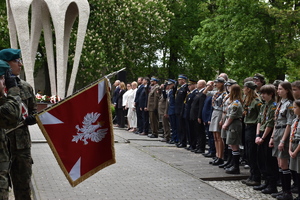 Zdjęcie w kolorze przedstawia na pierwszym planie Sztandar z Orłem Białym, w oddali zgromadzeni na uroczystości mieszkańcy oraz delegacje.