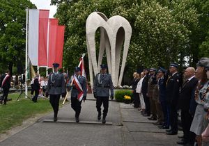 Zdjęcie w kolorze, przedstawia poczet sztandarowy KPP w Oleśnie odchodzący od pomnika. Po lewej stronie biało czerwone flagi, po prawej mieszkańcy i delegacje.