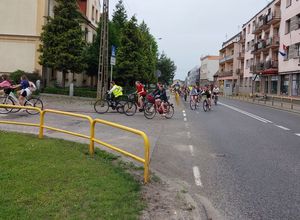 Zdjęcie w kolorze przedstawia rowerzystów jadących ulicą pośród miejskich zabudowań.