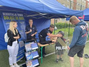 Zdjecie w kolorze, pzedstawia kilka osób w różnym wieku przy stoisku policyjnym.