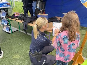 Zdjęcie w kolorze, przedstawia dziewczynkę która spogląda na obrazek w książce trzymanej w dłoniach przez policjantkę.