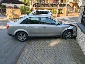 Zdjęcie w kolorze, przedstawia osobowe audi w kolorze szary metalik stojące na chodniku z przodem rozbitym na betonowym ogrodzeniu.
