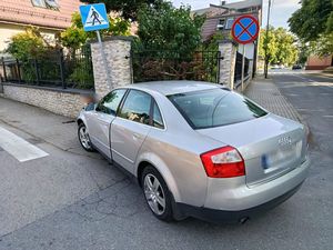Zdjęcie w kolorze, przedstawia osobowe audi w kolorze szary metalik stojące na chodniku z przodem rozbitym na betonowym ogrodzeniu.
