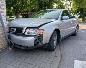 Zdjęcie w kolorze, przedstawia osobowe audi w kolorze szary metalik stojące na chodniku z przodem rozbitym na betonowym ogrodzeniu.