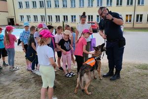 Zdjęcie w kolorze przedstawia policjanta z psem na dzieci głaszczą psa.