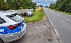 Ulica Kluczborska w Wojciechowie. W przydrożnym rowie stoi ciemny samochód osobowy. Widać uszkodzony betonowy płot posesji. Po lewej stronie na pierwszym planie tylna część policyjnego radiowozu policjantów ruchu drogowego.