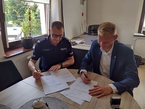 Zdjęcie w kolorze przedstawia jak Komendant Powiatowy Policji w Oleśnie i Wójt Gminy Zębowic podpisują dokumenty przy stole.