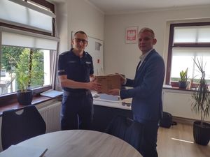 Zdjęcie w kolorze przedstawia jak Komendant Powiatowy Policji w Oleśnie odbiera karton z narkotestami od Wójta Gminy Zębowic w gabinecie Wójta.