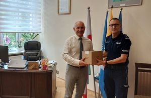 Zdjęcie w kolorze przedstawia jak Komendant Powiatowy Policji w Oleśnie odbiera karton z narkotestami od Burmistrza Olesna.