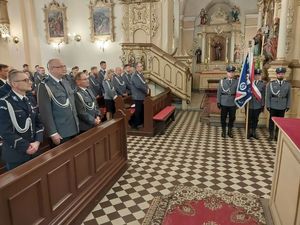 Zdjęcie w kolorze, przedstawia policjantów w umundurowaniu galowym od lewej siedzących w kościelnych ławkach, na wprost stoją trzej policjanci Pocztu sztandarowego Oleskiej Komendy.