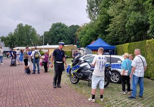 Zdjęcie w kolorze przedstawia kilka osób odwiedzających stoisko policyjne. kilka osób stoi przy motocyklu.