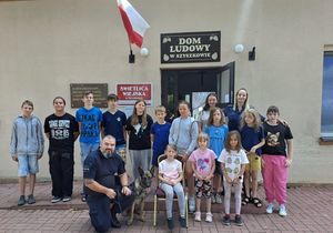 Zdjęcie w kolorze, dzieci i policjantów pozujących do zdjęcia przed wejściem do Świetlicy w Szyszkowie.