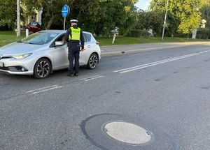 Zdjęcie w kolorze przedstawia  na jezdni policjant kontroluje trzeźwość kierującego pojazdem osobowym.