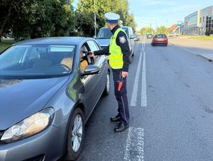 Zdjęcie w kolorze przedstawia na jezdni policjant kontroluje trzeźwość kierującego pojazdem osobowym.