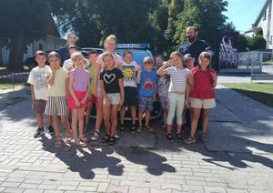 Zdjęcie w kolorze, przedstawia grupę dzieci pozujących do wspólnego zdjęcia z policjantami na tle radiowozu.