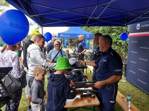 Zdjęcie w kolorze przedstawia uczestników dożynek w różnym wieku przy  stoisku policyjnym.