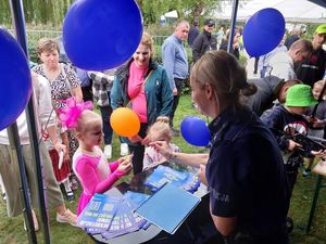 Zdjęcie w kolorze przedstawia, policjantkę wręczająca niebieski balon z napisem policja dla dziewczynki w wieku około 6 lat.