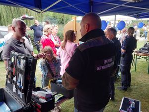 Zdjęcie w kolorze przedstawia uczestników imprezy odwiedzających policyjne stoisko promocyjne. Na pierwszym planie stanowisko technika kryminalistyki.