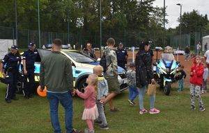 Zdjęcie w kolorze przedstawia uczestników imprezy odwiedzających policyjne stoisko z pojazdami w tle miasteczko ruchu drogowego dla najmłodszych.