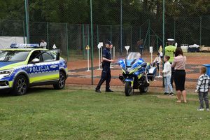 Zdjęcie w kolorze przedstawia uczestników imprezy odwiedzających stoisko policyjne z pojazdami.